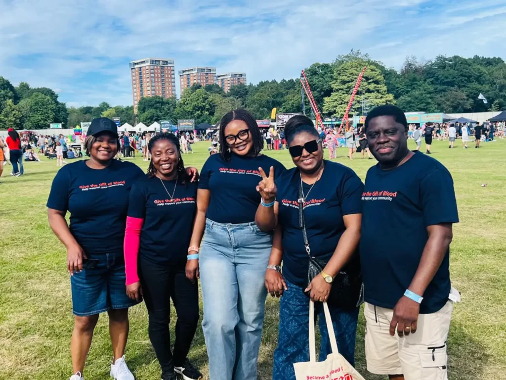Five team members in matching navy T-shirts stand together on a sunny park field at a community event